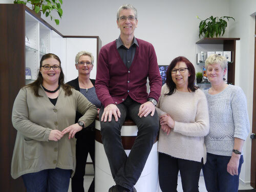 Fünfköpfiges Praxisteam steht gemeinsam freundlich lächelnd in moderner Arztpraxis.